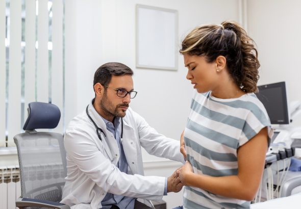 Patient telling physician about her pain and health problems during visit to hospital. Young woman complaining about back or kidney ache while sitting on examination bed at the doctor's office