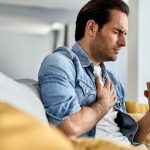 Young man having a chest pain while drinking tea at home.