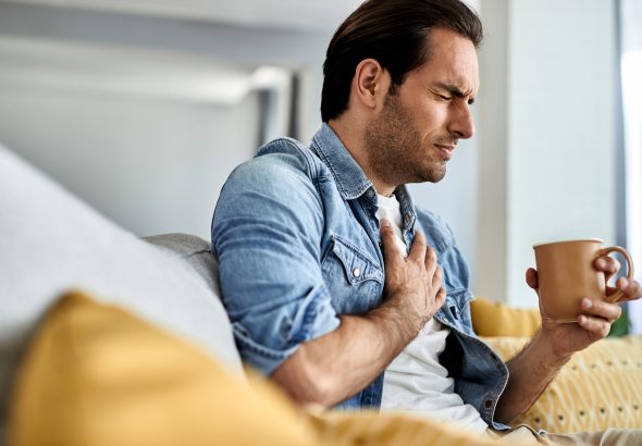 Young man having a chest pain while drinking tea at home.